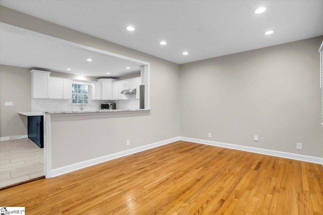 kitchen with sink, light stone counters, kitchen peninsula, white cabinets, and light wood-type flooring