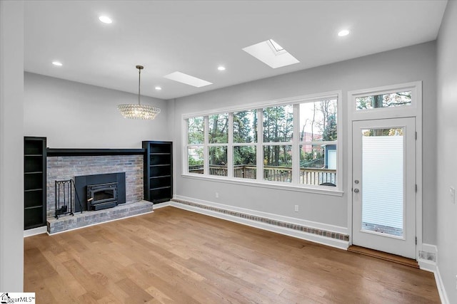 unfurnished living room with a notable chandelier, a skylight, a wealth of natural light, and light hardwood / wood-style flooring