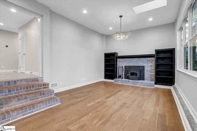 unfurnished living room with hardwood / wood-style flooring, a wood stove, a skylight, and a notable chandelier