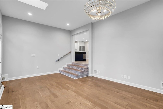 unfurnished living room featuring a notable chandelier, a skylight, and light hardwood / wood-style flooring