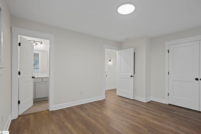 unfurnished bedroom with ensuite bath, a closet, and dark hardwood / wood-style flooring