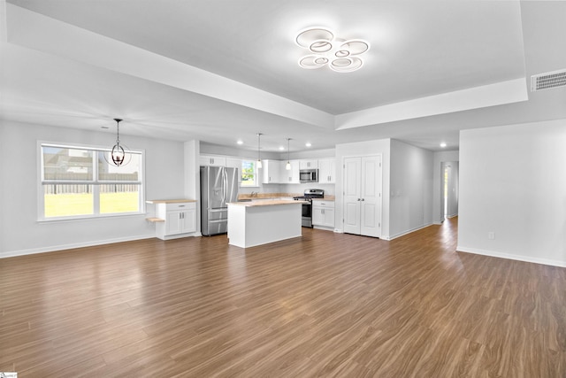 unfurnished living room with plenty of natural light, an inviting chandelier, dark hardwood / wood-style flooring, and a tray ceiling