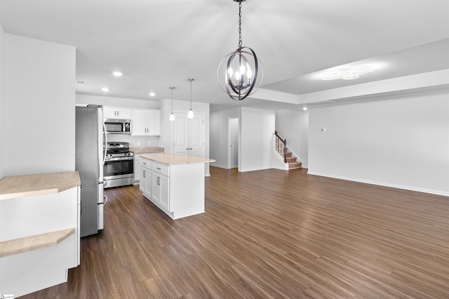 kitchen with dark wood-type flooring, white cabinets, pendant lighting, a kitchen island, and appliances with stainless steel finishes