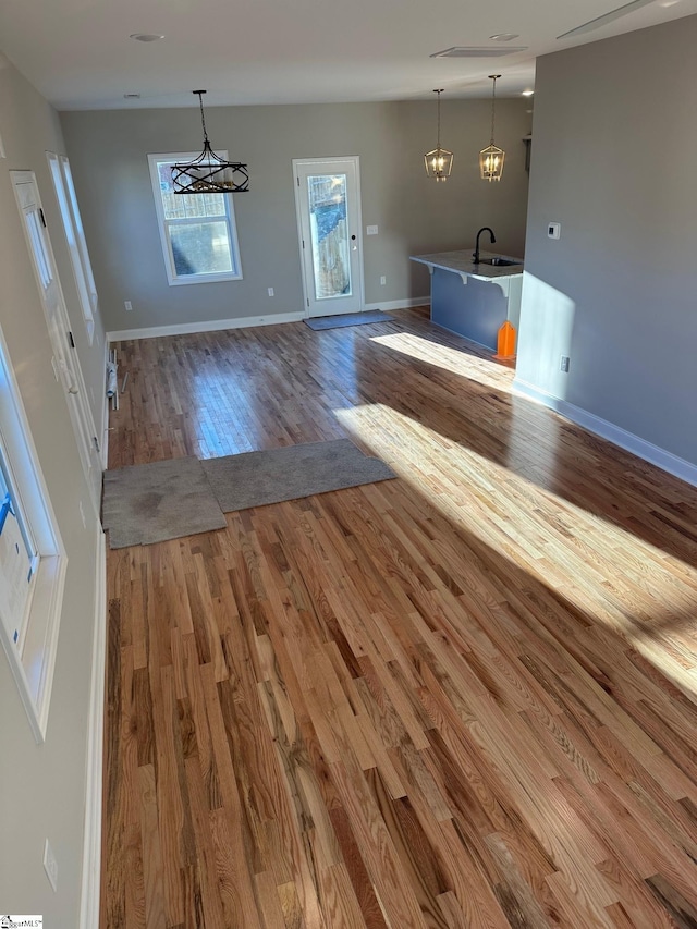 unfurnished living room with hardwood / wood-style flooring, sink, and an inviting chandelier