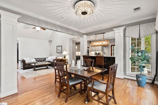 dining room featuring bar area, crown molding, ceiling fan, light wood-type flooring, and decorative columns