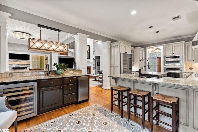 kitchen with appliances with stainless steel finishes, light hardwood / wood-style floors, a stone fireplace, and beverage cooler