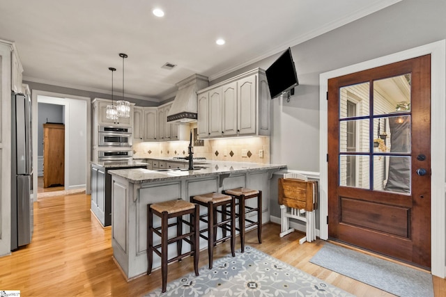 kitchen with gray cabinets, light wood-type flooring, tasteful backsplash, light stone counters, and custom range hood