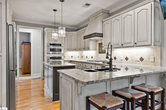 kitchen with light stone countertops, stainless steel appliances, backsplash, custom range hood, and light wood-type flooring