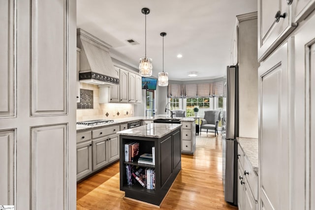 kitchen with a center island, stainless steel appliances, pendant lighting, light hardwood / wood-style floors, and custom range hood