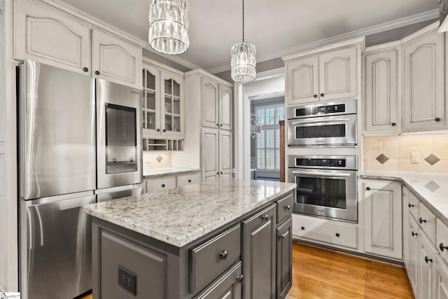 kitchen with backsplash, light wood-type flooring, appliances with stainless steel finishes, a notable chandelier, and a kitchen island