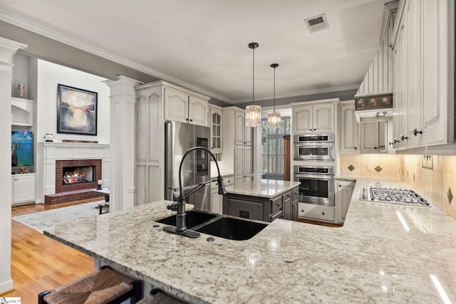 kitchen with a brick fireplace, backsplash, kitchen peninsula, wood-type flooring, and appliances with stainless steel finishes