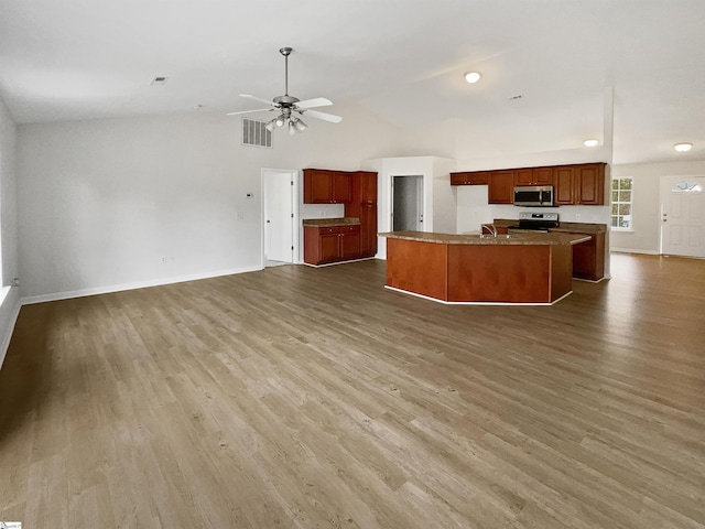 kitchen with hardwood / wood-style flooring, a kitchen island with sink, appliances with stainless steel finishes, and vaulted ceiling