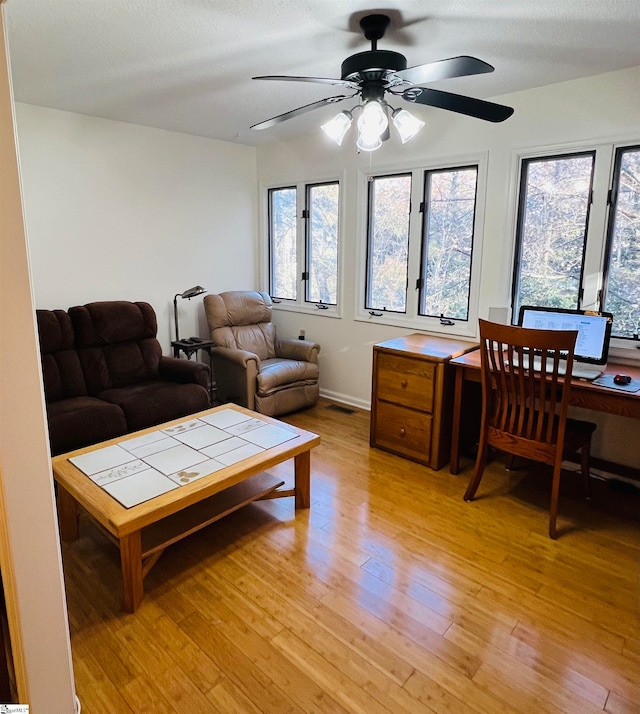 living room featuring ceiling fan, light wood-type flooring, and a textured ceiling