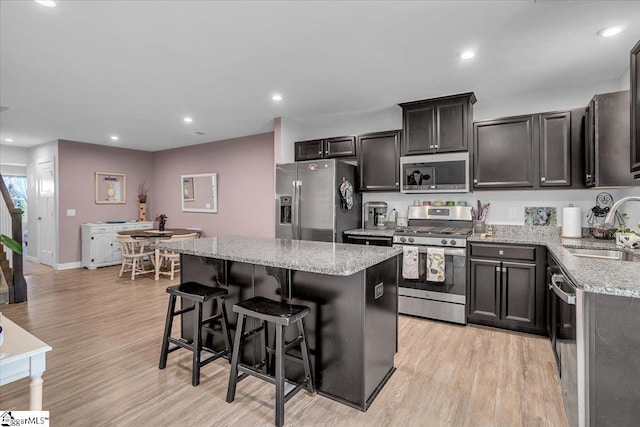 kitchen with light stone countertops, appliances with stainless steel finishes, light wood-type flooring, sink, and a kitchen island