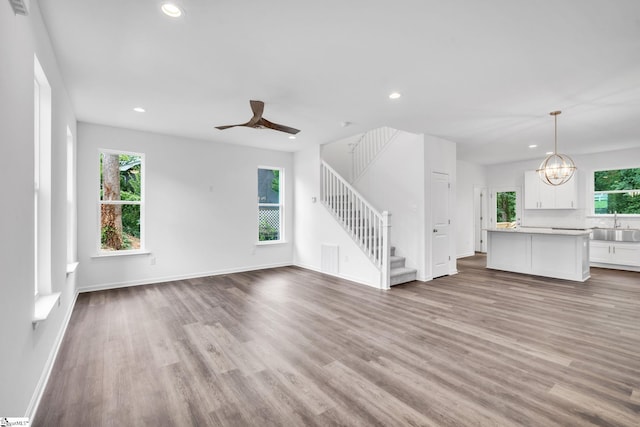 unfurnished living room with ceiling fan with notable chandelier, light wood-type flooring, and sink