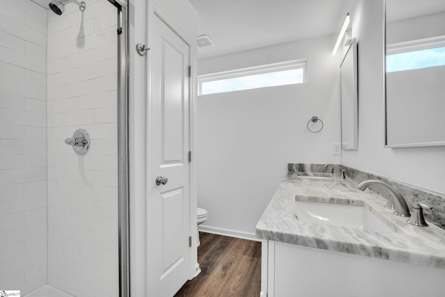 bathroom with a tile shower, hardwood / wood-style floors, vanity, and toilet