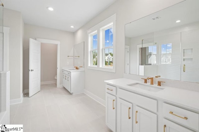 bathroom featuring toilet, a sink, a stall shower, baseboards, and two vanities
