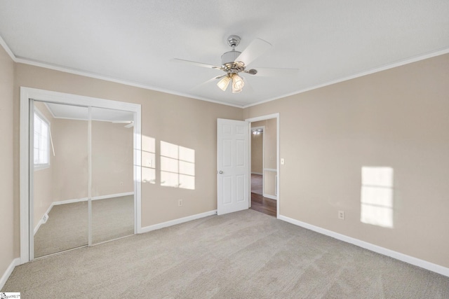 unfurnished bedroom featuring crown molding, ceiling fan, a closet, and light colored carpet