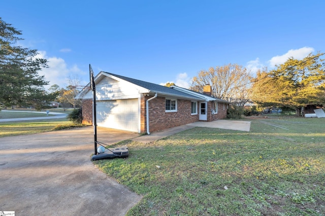 view of side of property featuring brick siding, a chimney, a yard, a garage, and driveway