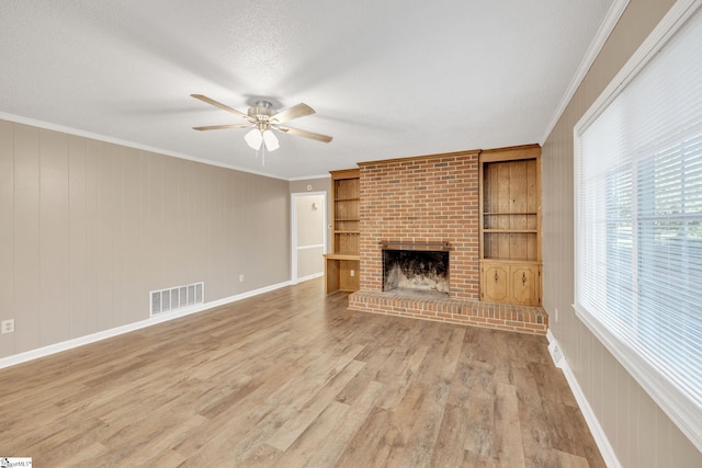 unfurnished living room featuring wood-type flooring, a brick fireplace, ceiling fan, and ornamental molding