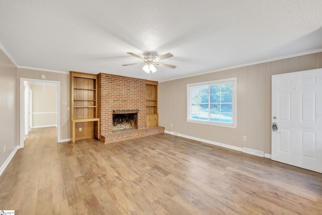 unfurnished living room with ceiling fan, crown molding, a textured ceiling, a fireplace, and light wood-type flooring