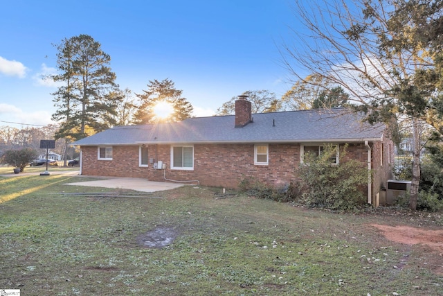 rear view of property featuring a lawn, a patio, roof with shingles, brick siding, and a chimney