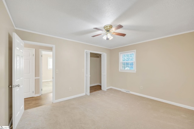 unfurnished bedroom featuring a textured ceiling, light colored carpet, ceiling fan, crown molding, and a closet