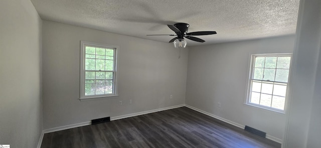 empty room with a textured ceiling, a healthy amount of sunlight, and dark hardwood / wood-style floors