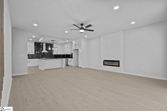 unfurnished living room with ceiling fan, a large fireplace, and light hardwood / wood-style flooring