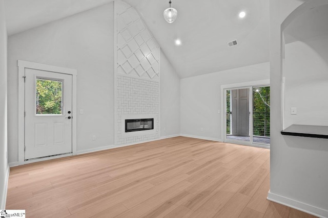 unfurnished living room featuring a fireplace, high vaulted ceiling, and light hardwood / wood-style floors