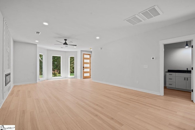 unfurnished living room with heating unit, light hardwood / wood-style floors, and ceiling fan