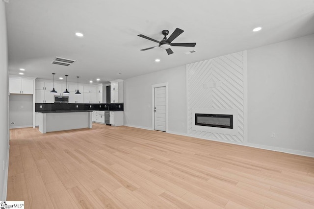 unfurnished living room featuring light wood-type flooring, a large fireplace, and ceiling fan