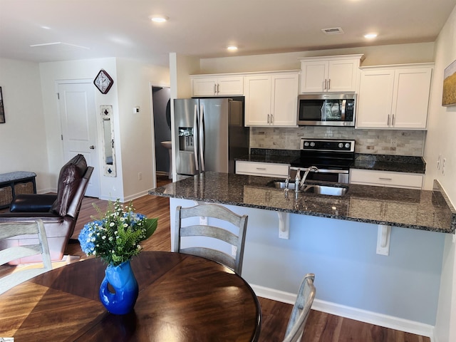 kitchen featuring backsplash, white cabinets, dark hardwood / wood-style floors, appliances with stainless steel finishes, and a breakfast bar area