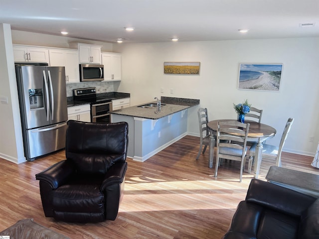 kitchen featuring sink, appliances with stainless steel finishes, light hardwood / wood-style floors, a kitchen bar, and white cabinetry