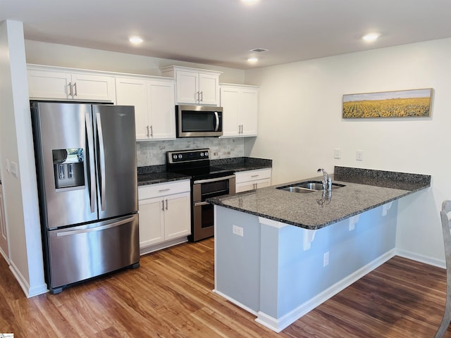 kitchen with sink, kitchen peninsula, hardwood / wood-style floors, white cabinets, and appliances with stainless steel finishes