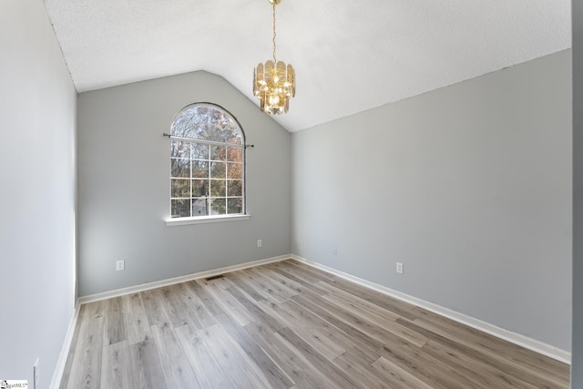 unfurnished room with a textured ceiling, a notable chandelier, lofted ceiling, and light wood-type flooring