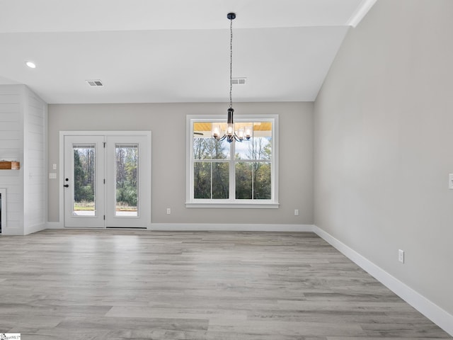 unfurnished dining area featuring a large fireplace, a chandelier, vaulted ceiling, and light wood-type flooring