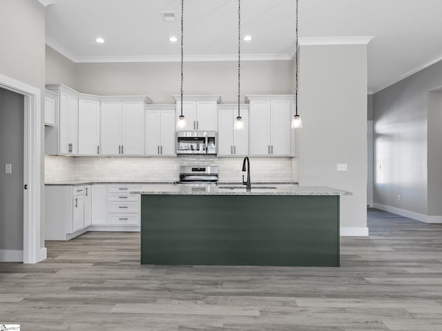 kitchen featuring a kitchen island with sink, appliances with stainless steel finishes, decorative light fixtures, light stone counters, and white cabinetry