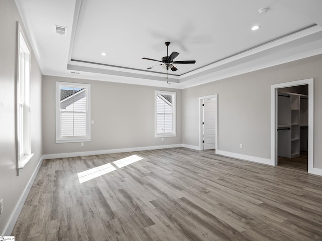 interior space featuring ceiling fan, a walk in closet, multiple windows, and a tray ceiling