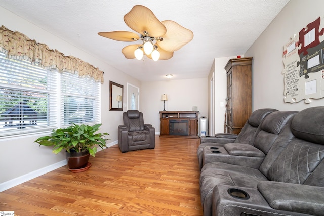 living room with ceiling fan, a textured ceiling, and light hardwood / wood-style floors