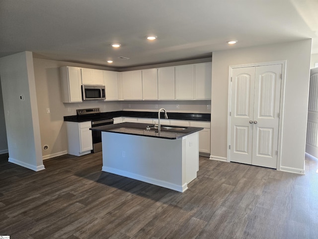 kitchen featuring white cabinets, stainless steel appliances, dark wood-type flooring, and an island with sink