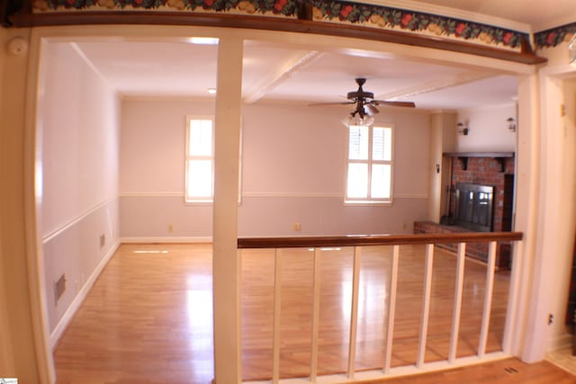 interior space with beamed ceiling, a brick fireplace, hardwood / wood-style floors, and ceiling fan