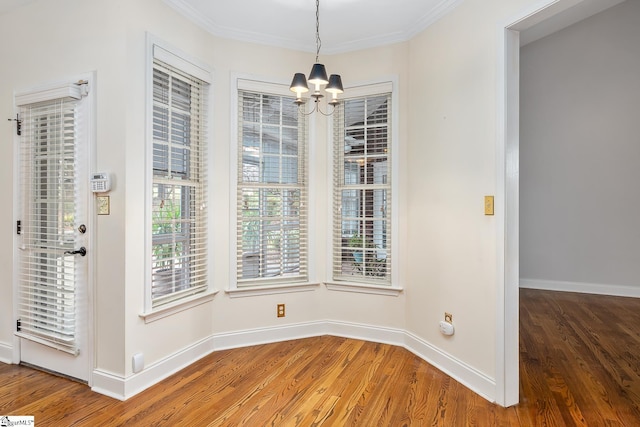 unfurnished dining area with hardwood / wood-style floors, crown molding, and an inviting chandelier