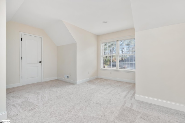 additional living space featuring light colored carpet and vaulted ceiling