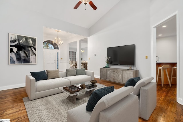 living room with ceiling fan with notable chandelier, hardwood / wood-style flooring, high vaulted ceiling, and crown molding