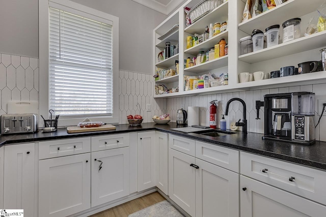 kitchen with white cabinetry, sink, tasteful backsplash, light hardwood / wood-style flooring, and ornamental molding