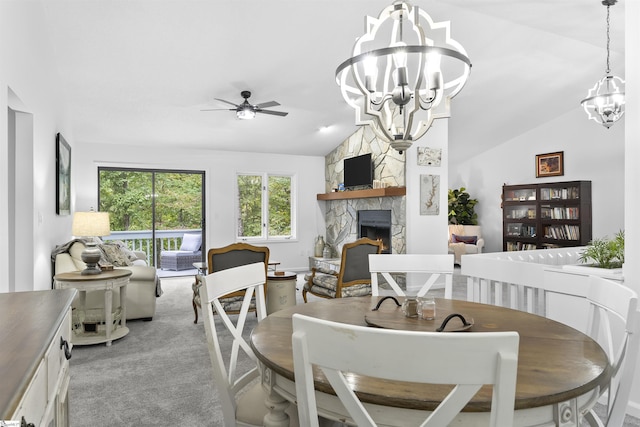 carpeted dining space featuring ceiling fan with notable chandelier, vaulted ceiling, and a stone fireplace