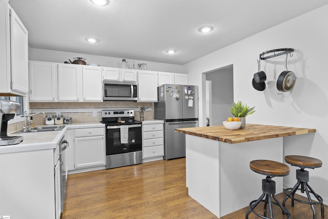 kitchen featuring sink, light wood-type flooring, appliances with stainless steel finishes, a kitchen bar, and white cabinetry