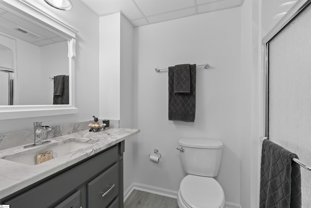 bathroom featuring a paneled ceiling, vanity, hardwood / wood-style flooring, toilet, and a shower with shower door