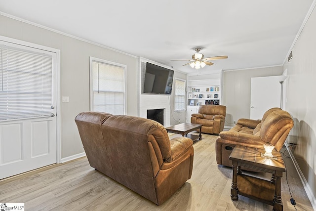 living room with ceiling fan, a large fireplace, light wood-type flooring, and ornamental molding